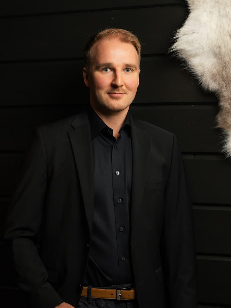 Olli Salmela in a dark blazer against a black timber wall